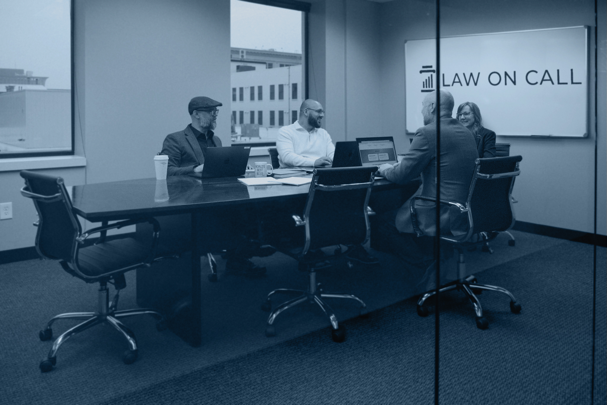 Four people sitting at a conference table in an office setting with "Law on Call" logo projected on a screen behind them.