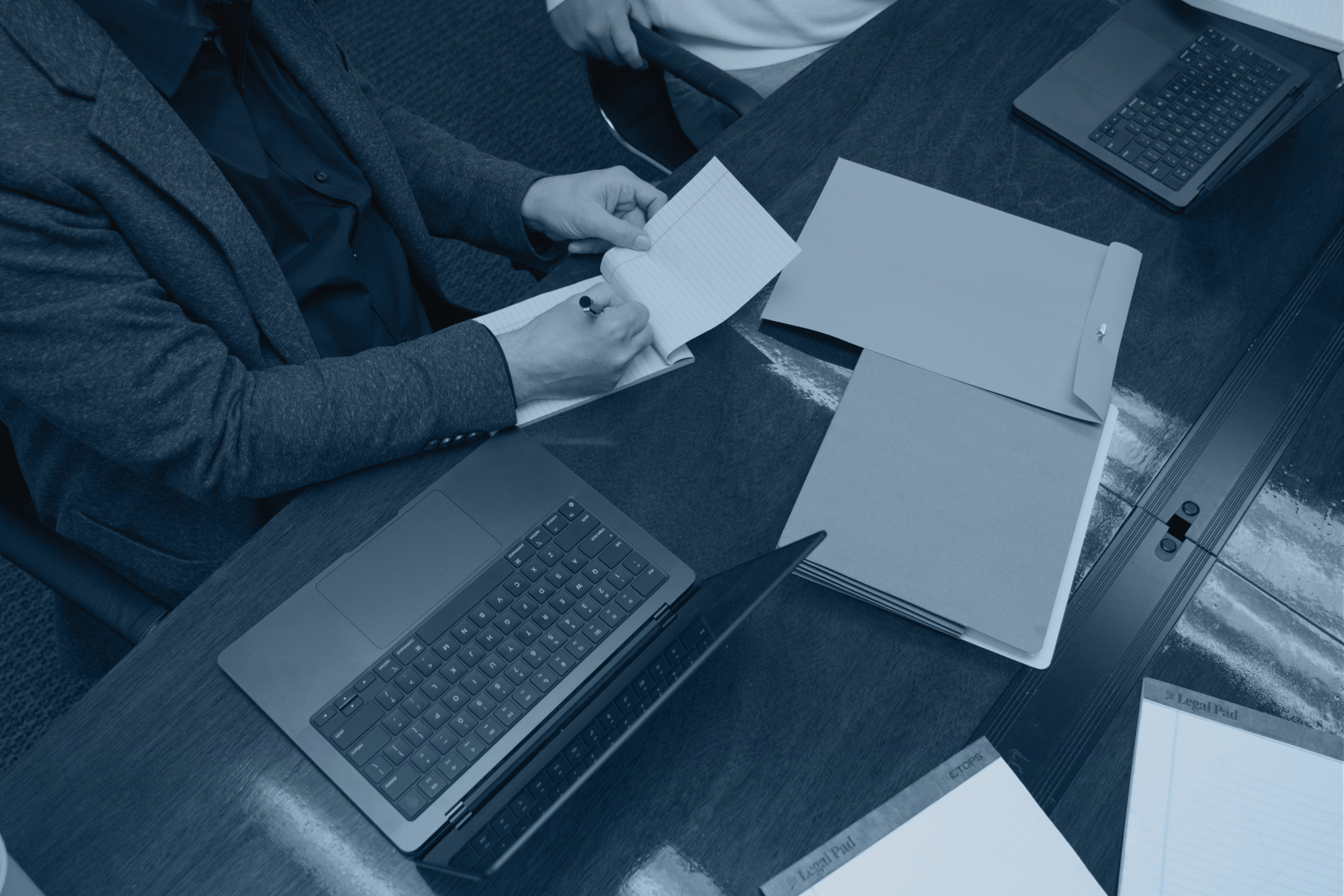 Person writing in a notepad at a desk next to an open laptop.