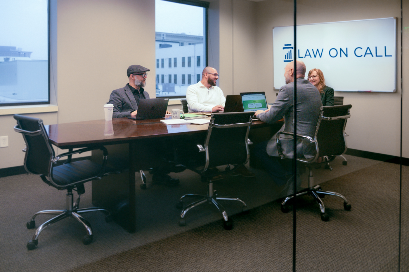 Four people sitting at a conference table in an office setting with "Law on Call" logo projected on a screen behind them.