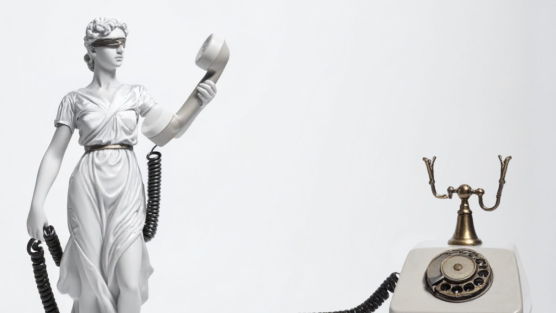 Blindfolded Lady Justice statue holding a telephone receiver beside a vintage rotary phone.